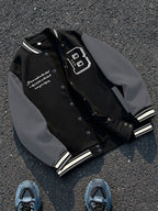This Black And Gray Patchwork Baseball Jacket Features a Button Closure Design, with Black And White Striped Accents at The Collar And Cuffs. It Showcases Prominent Letter Prints And English Text Elements on The Chest - Black And Grey
